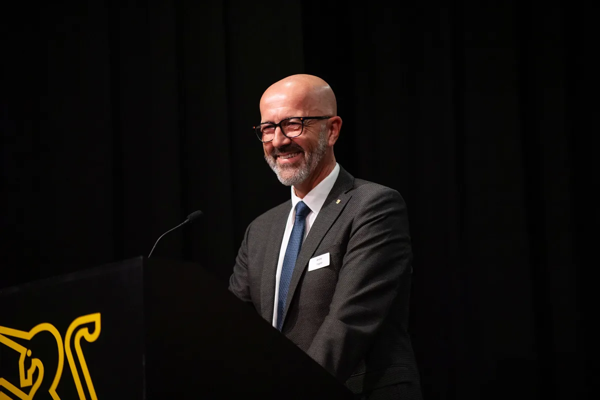 Ein Mann im Anzug steht vor einem Mikrofon und lacht. 